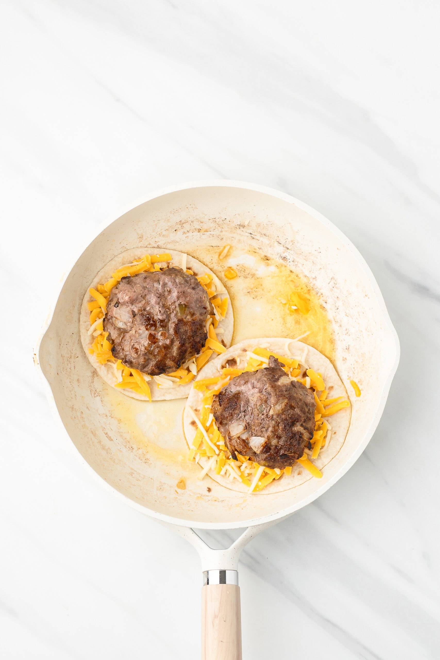 Burgers placed on top of cheeses on a tortilla in a buttered skillet