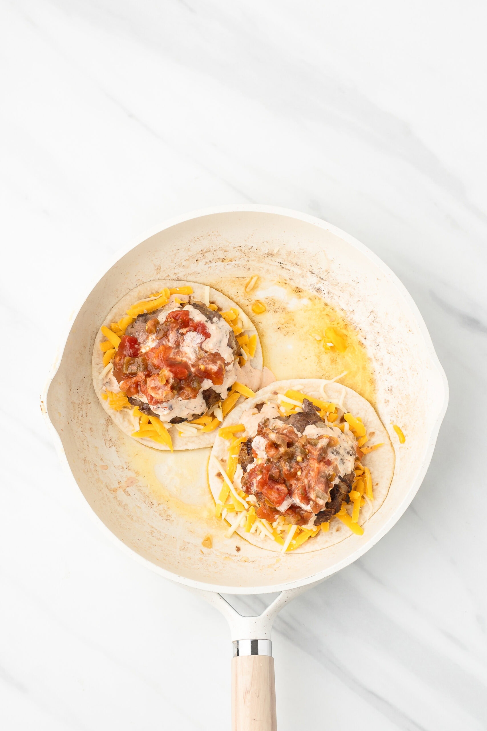 Burgers placed on top of tortilla with cheese, mayo and salsa in a skillet