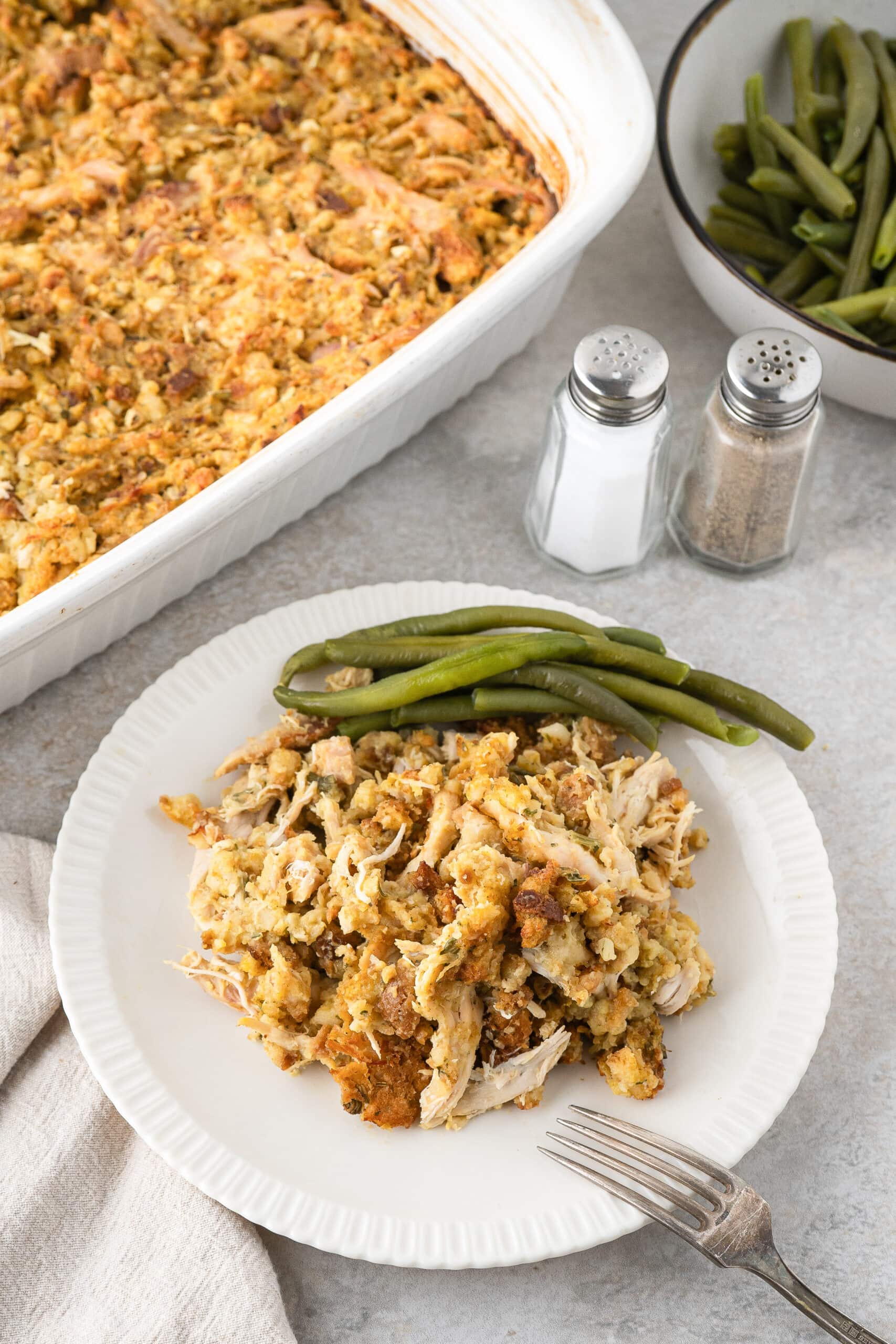 Stove top stuffing and rotisserie chicken casserole on a plate with a side of green beans, fork is there to enjoy the meal