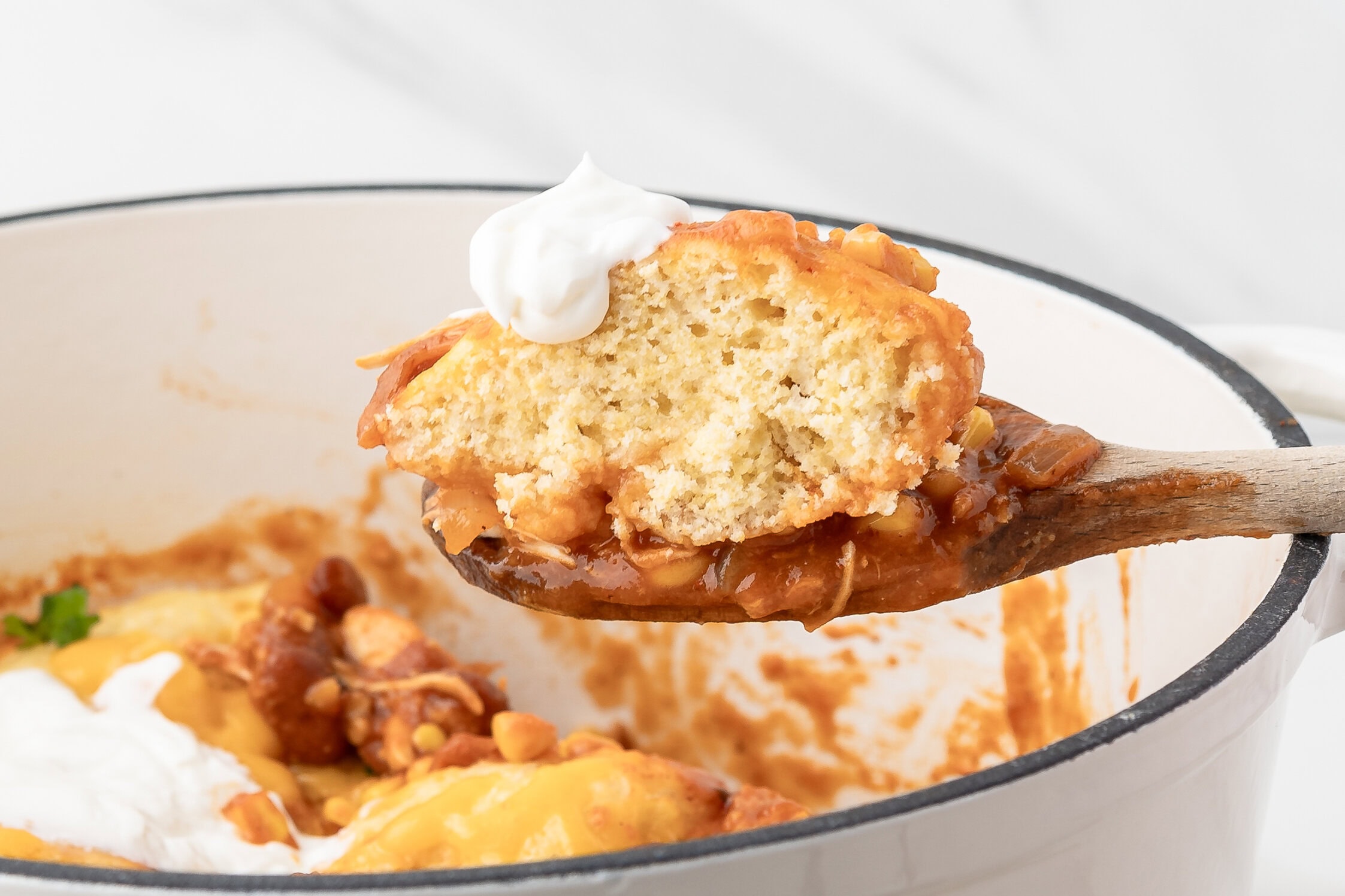 A wooden spoon showing a scoop of chicken chili with a dumpling on top