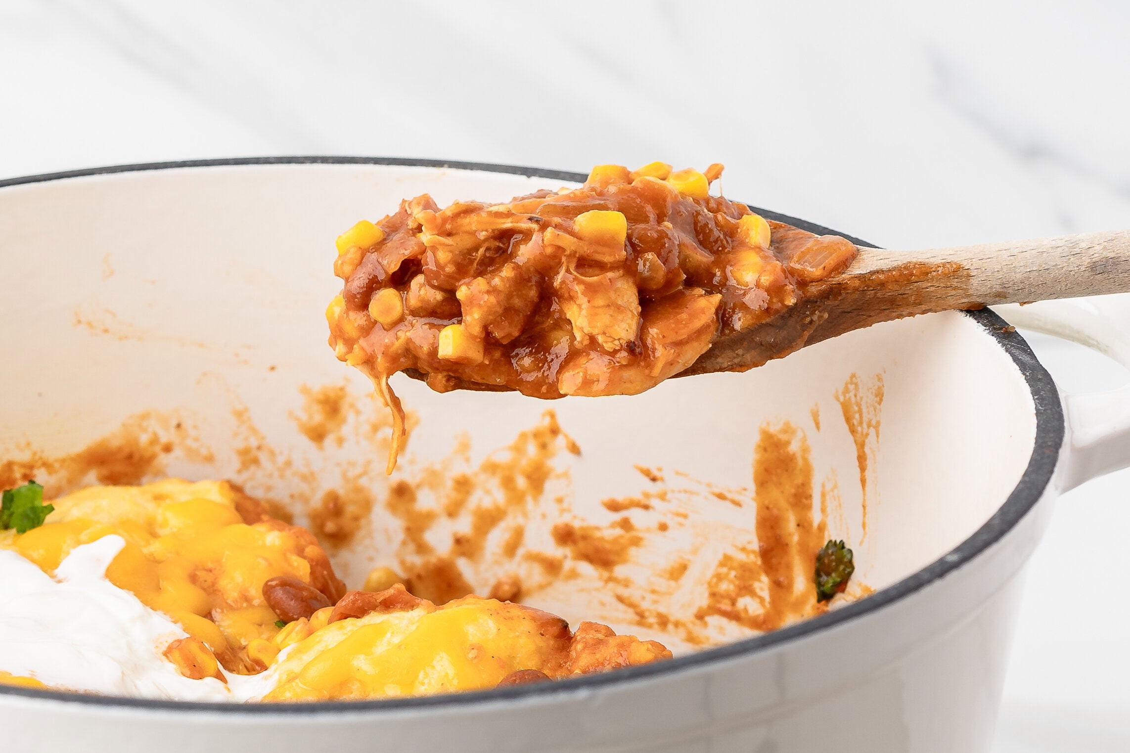 A wooden spoon holding up a scoop of chicken chili with dumplings