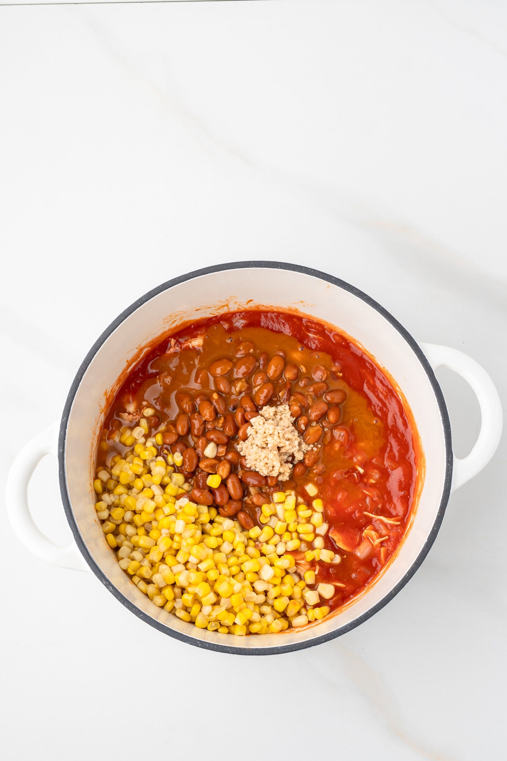 Corn, chili beans and garlic are being added to the chicken and tomato sauce in dutch oven