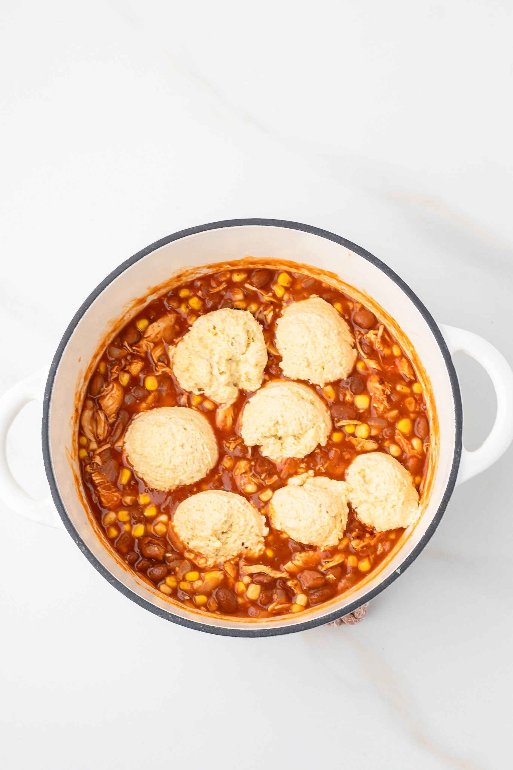 The dumplings are dropped into the dutch oven on top of the chicken chili in dutch oven