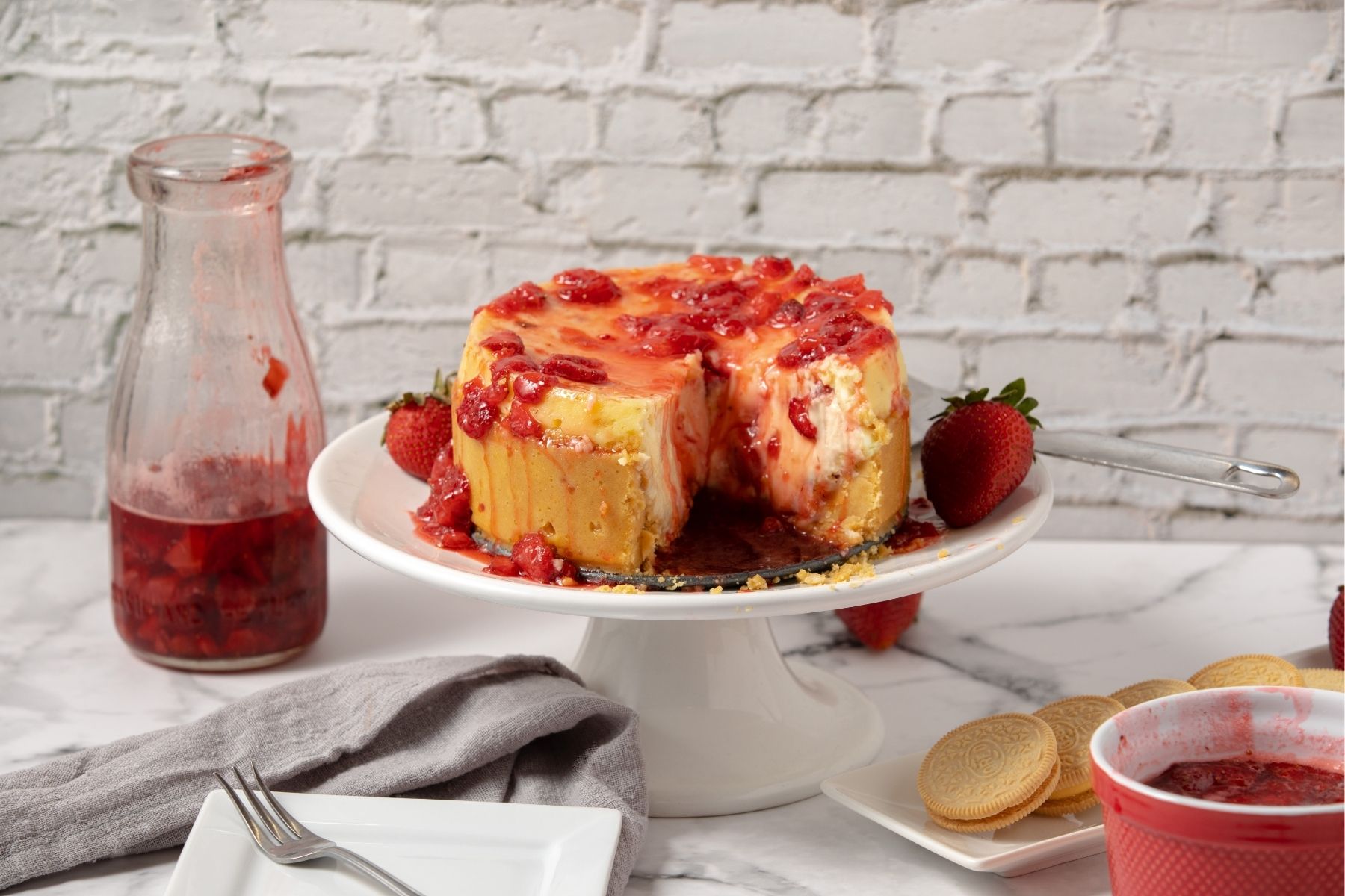 Instant Pot strawberry cheesecake topped with strawberry sauce on cake stand
