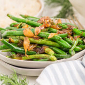 sauteed green beans topped with caramelized onions and fresh dill on a white plate