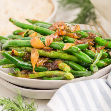 sauteed green beans topped with caramelized onions and fresh dill on a white plate