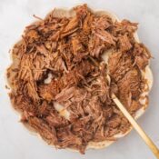 crockpot bbq pulled beef in a tan colored bowl with a gold spoon
