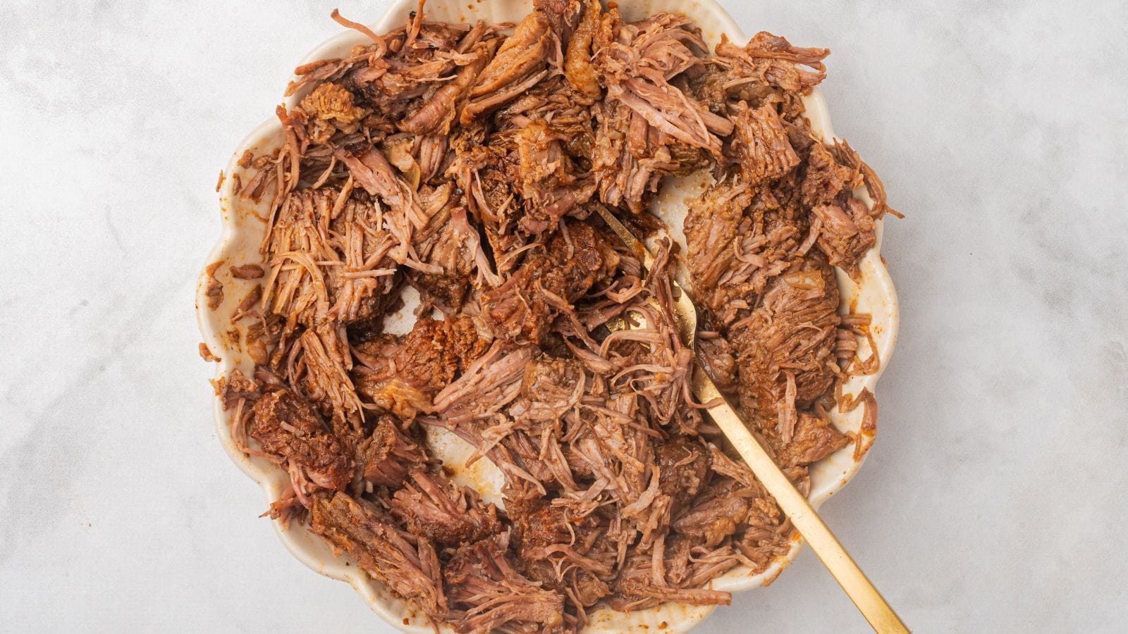 a bowl full of crockpot bbq pulled beef with a gold spoon