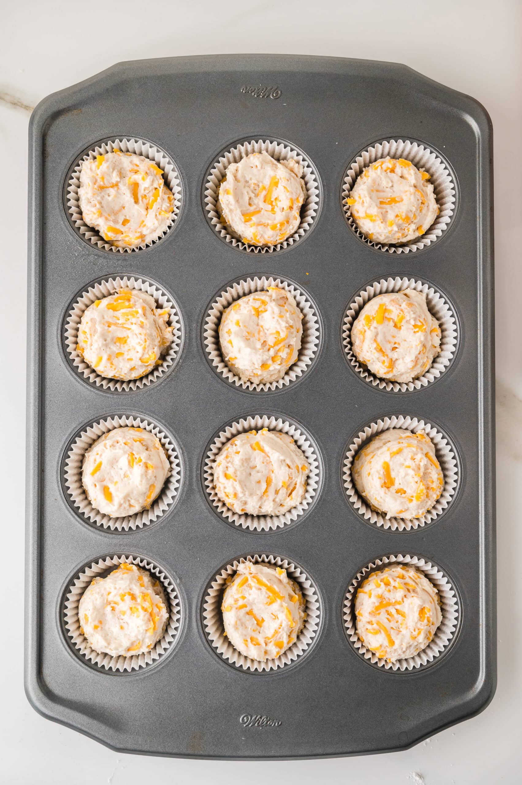 Unbaked cheddar cheese muffins in a muffin tin