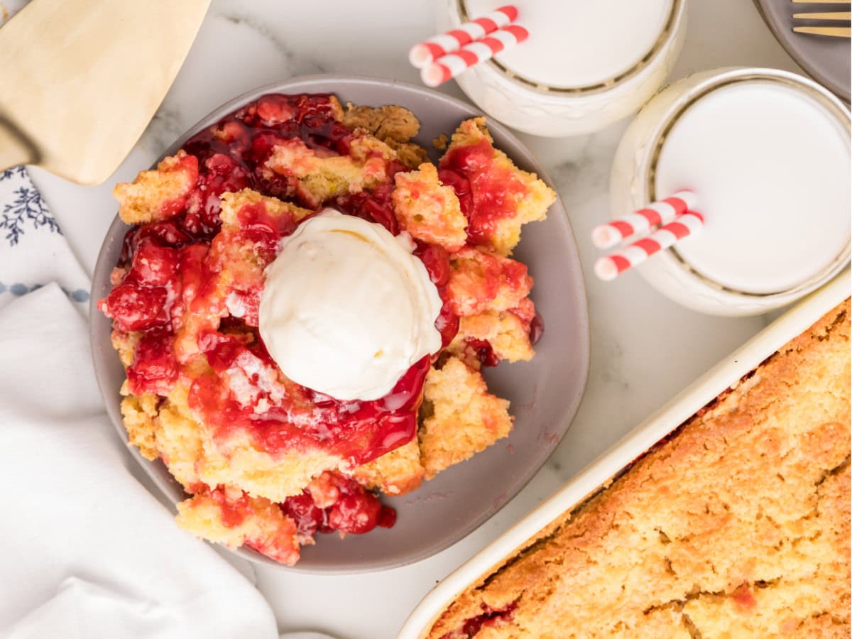 Cherry dump cake with vanilla ice cream and milk glasses on a table.